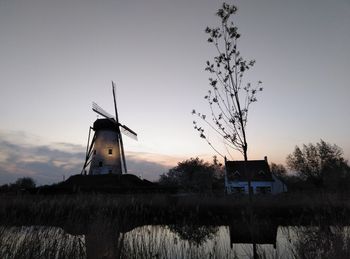 Traditional windmill by building against sky during sunset