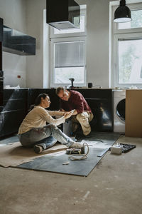 Full length of couple discussing over mobile phone while renovating kitchen at home