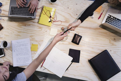 Directly above shot of woman giving pen to colleague at wooden desk