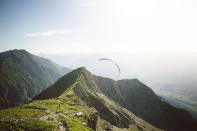 Scenic view of mountains with person paragliding against sky