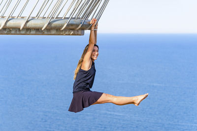 Happy mature woman hanging on railing while practicing acrobatics at viewpoint