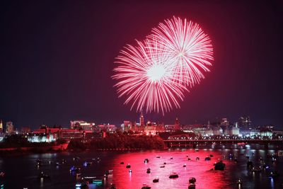 Firework display over illuminated city against sky at night