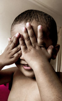 Close-up portrait of shirtless boy covering face