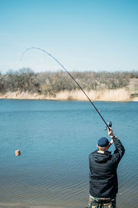 Rear view of man fishing in sea against sky