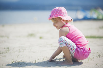 Cute girl looking down while crouching at beach on sunny day
