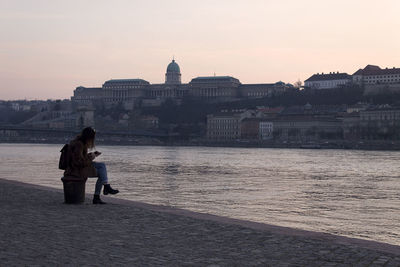 Woman looking at river in city against sky