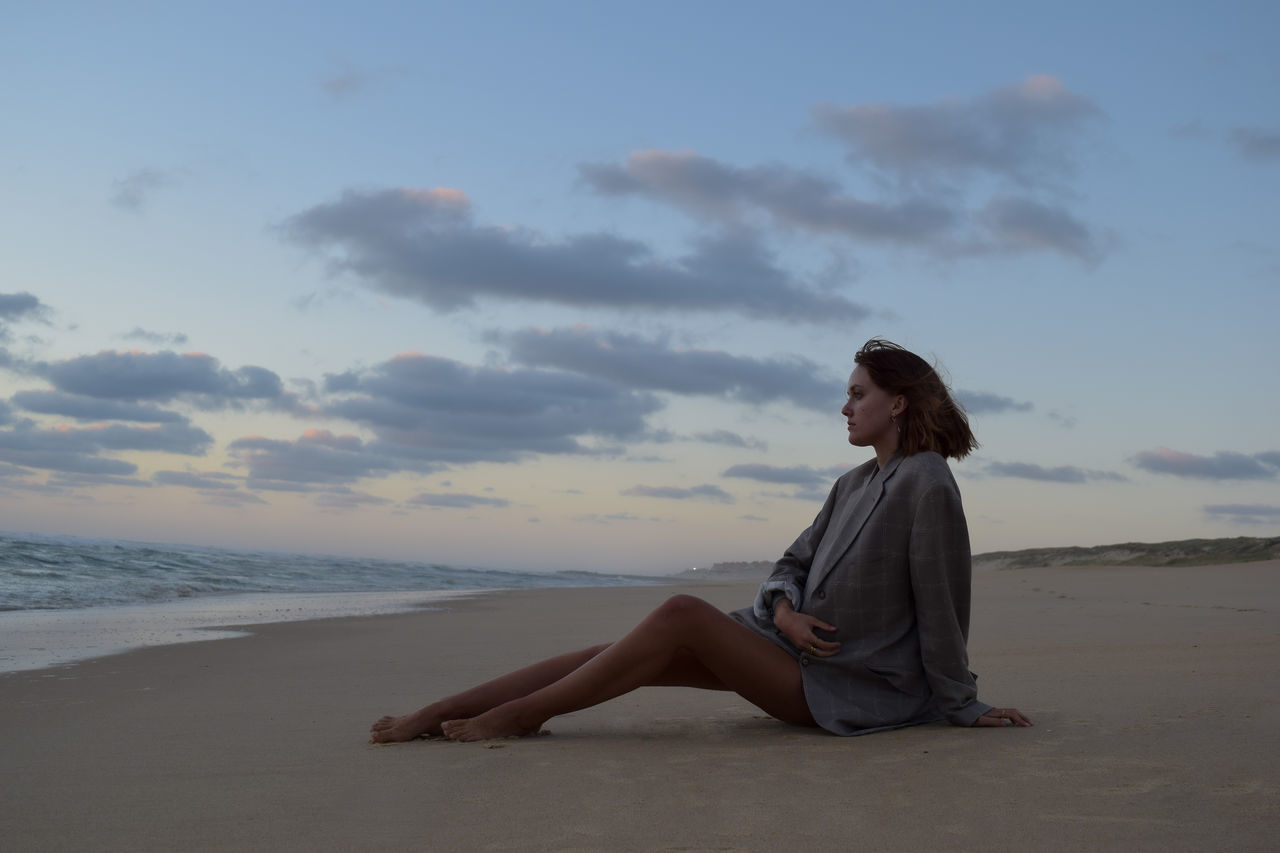 sky, land, one person, beach, sea, water, adult, full length, nature, horizon, sand, cloud, ocean, sitting, relaxation, women, tranquility, young adult, beauty in nature, leisure activity, side view, holiday, vacation, shore, trip, horizon over water, solitude, coast, contemplation, sunlight, lifestyles, tranquil scene, wave, morning, barefoot, scenics - nature, clothing, casual clothing, looking, body of water, outdoors, hairstyle, copy space, idyllic, environment, female, dusk, day, travel