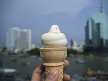 Hand holding ice cream cone against buildings in city