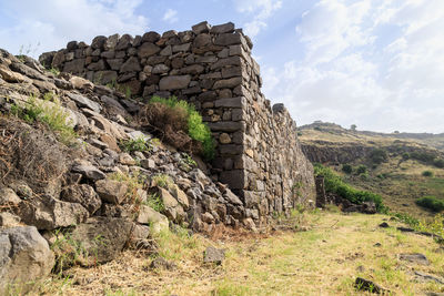 Stone wall by rocks against sky