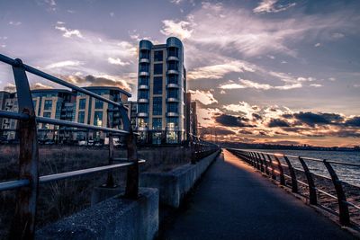 Bridge over footpath in city against sky during sunset