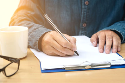 Midsection of man writing on paper on table