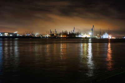 Illuminated city by sea against sky at night