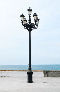 Street light on footpath by sea against sky