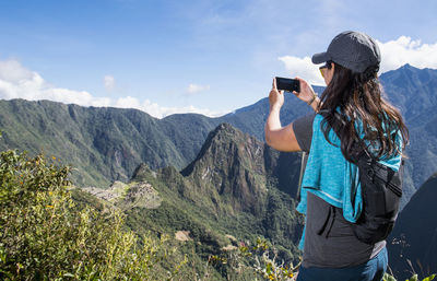 Man photographing with mobile phone against sky