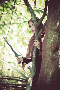Portrait of young woman holding weapon standing by tree trunk