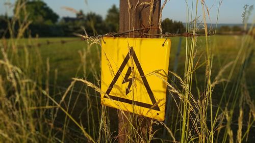 Close-up of yellow sign board on field by lake