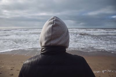 Rear view of person at beach against cloudy sky