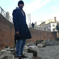 Portrait of young man standing on retaining wall against sky