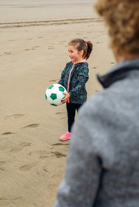 Woman standing with granddaughter holding soccer ball at beach