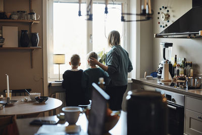 Rear view of mother with sons looking outside from kitchen window