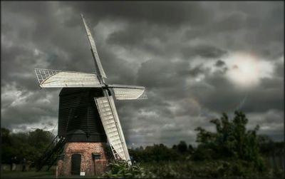 Traditional windmill on field against cloudy sky