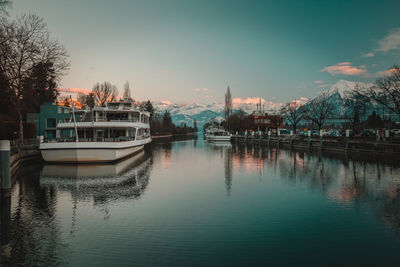 Boats moored in river against sky during sunset