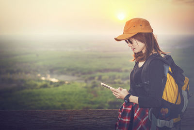 Young woman using smart phone against sky during sunset