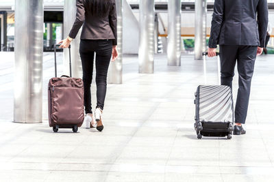 Low section of businesswoman and woman walking with luggage on footpath