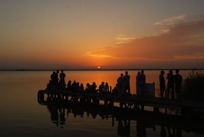 Silhouette people on pier over sea against sky during sunset