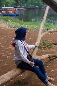 Rear view of woman sitting on land by lake