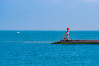 Lighthouse on sea against clear blue sky