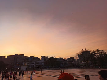 Group of people in city against sky during sunset