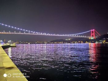 Illuminated bridge over river with city in background