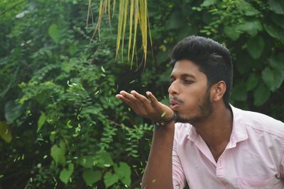 Young man blowing leaves while standing against plants at park