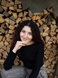 Portrait of smiling young woman crouching against stacked logs