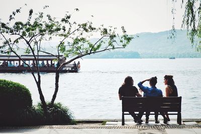 Rear view of people sitting on riverbank against sky