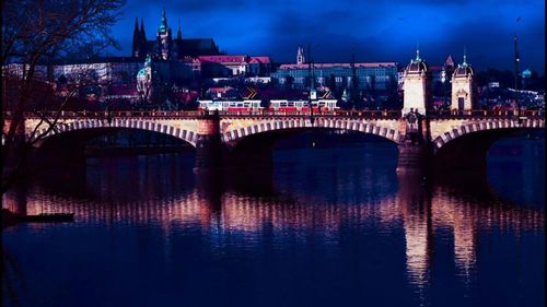 Illuminated bridge over river in city against sky at night