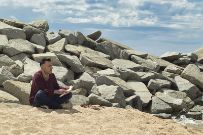 Man sitting on the sand reading a book on the seashore near a breakwater