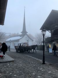 People walking on snow covered city against sky