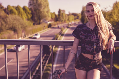 Portrait of young woman with long hair standing on footbridge over road