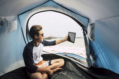 Teenage boy using digital tablet while sitting in tent 
