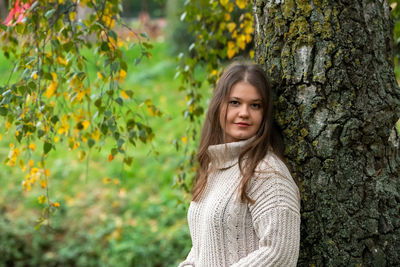 Portrait of young woman standing by tree trunk