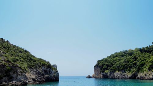 Rocky cliff with sea against clear sky