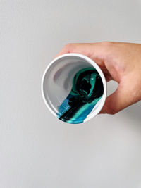 Hand holding a cup with an abstract layered paint pattern