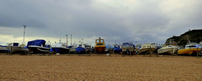 Boats moored at sandy beach against cloudy sky