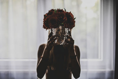 Woman holding flower pot in front face at home