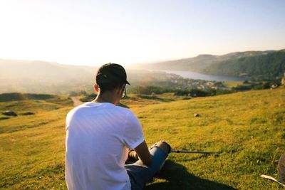 Rear view of man relaxing on grassy field during sunny day