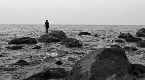 Man standing on rock by sea against clear sky