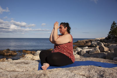 Woman sitting on rock at beach against sky