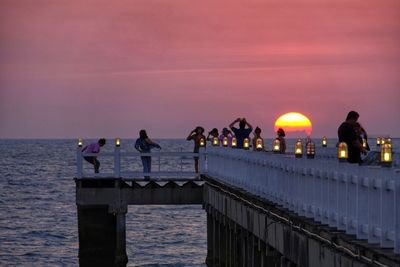 People on pier by sea against sky during sunset